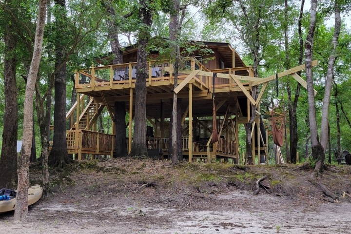 Elevated wooden cabin among trees with a canoe on the shore.