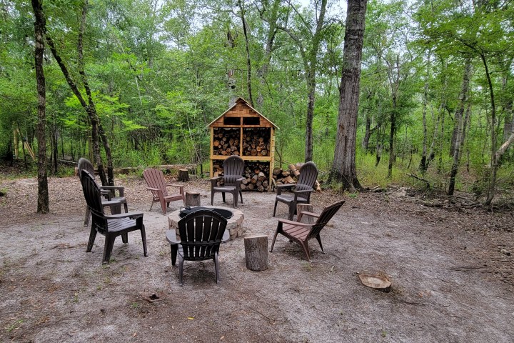 Outdoor fire pit with wooden chairs in a forest setting.