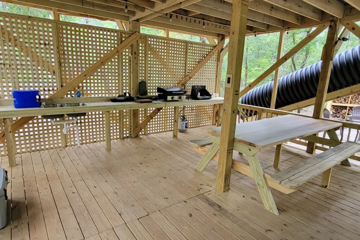 Wooden deck with picnic table and kitchen setup under lattice roof.
