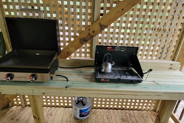 Outdoor cooking area with two burners and a kettle on a wooden table.
