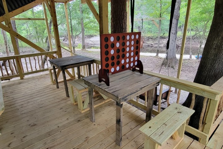 Wooden deck with table, large Connect Four game, and surrounding trees.
