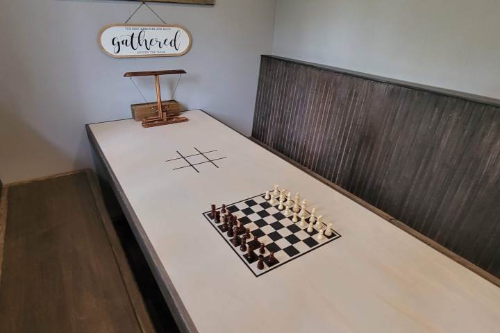 A chessboard with pieces on a table, tic-tac-toe drawn beside it, and a 'gathered' sign above.