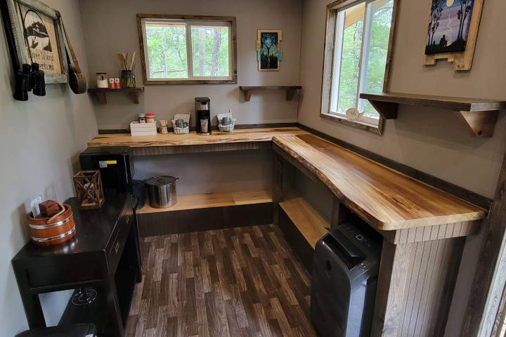 Rustic room with wooden countertops, shelves, and coffee machine, natural light from two windows.