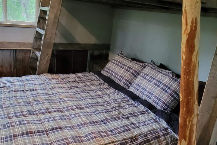 Room with rustic bunk bed and plaid bedding, wooden floor.