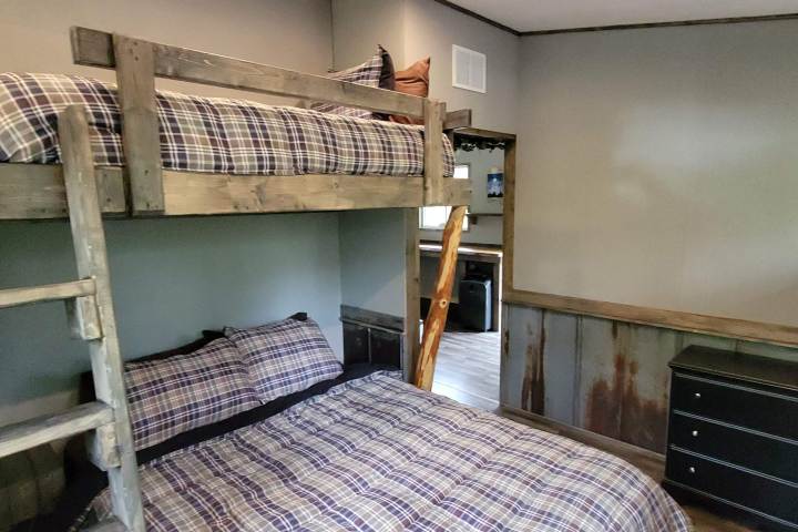 Room with wooden bunk bed and plaid bedspreads, dresser, and small workspace.