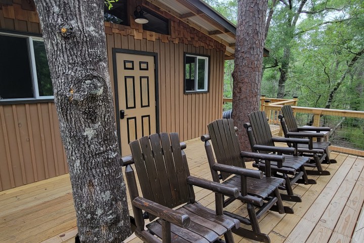 Wooden deck with chairs outside a brown cabin in a forested area.