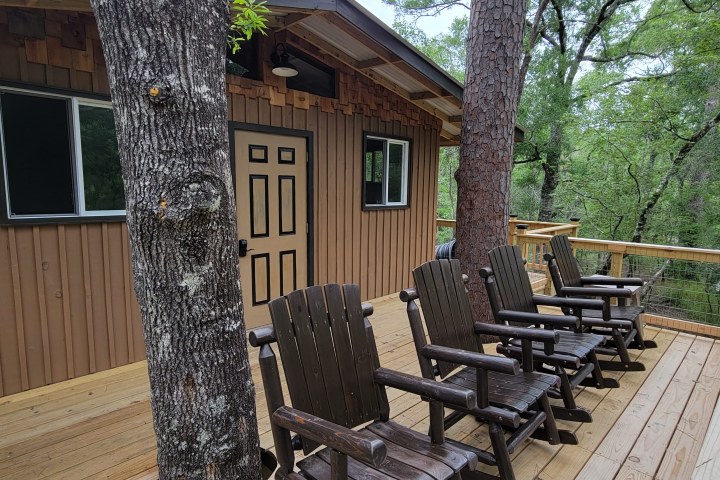 Wooden cabin with porch, chairs, and forest view.