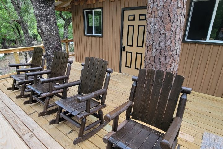 Wooden deck with four rocking chairs and tree trunks passing through it.