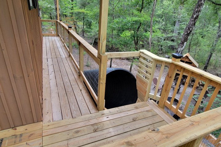 Wooden deck with railings, grill, surrounded by forest trees.