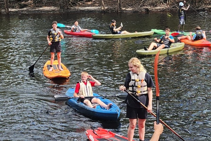 Group of people kayaking on a river surrounded by trees.