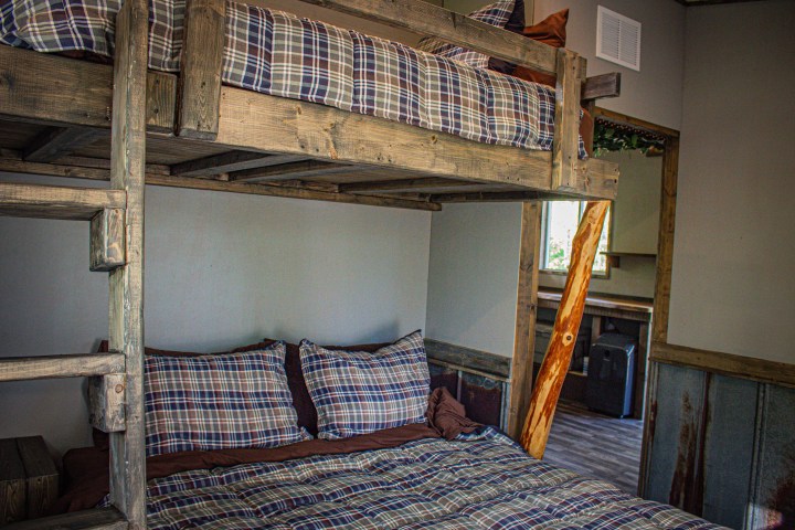 Wooden bunk bed with plaid bedding in a rustic room.