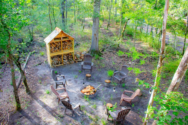 Chairs around a fire pit in a wooded area with a wood storage shed.
