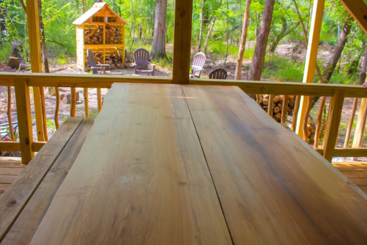 Wooden porch with table overlooking forest and chairs.