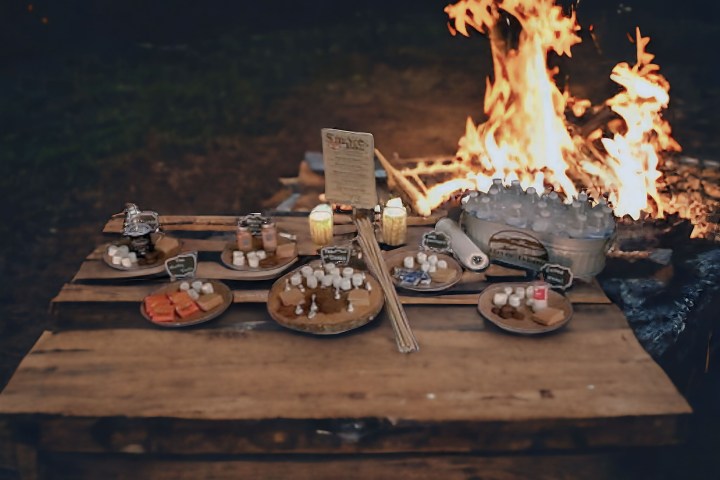 Wooden table with snacks near a campfire at night