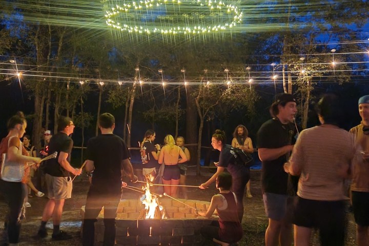 People gathered around a campfire under string lights at night.