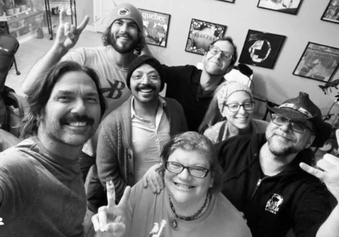 Group of seven people smiling and posing for a selfie indoors.